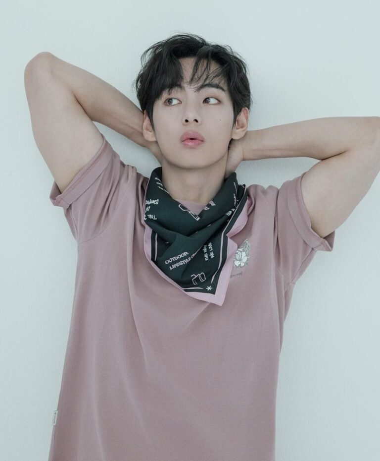 BTS member V in a global promotional portrait, posing in a minimalist setting with soft lighting, highlighting his fashion styling and international star presence.