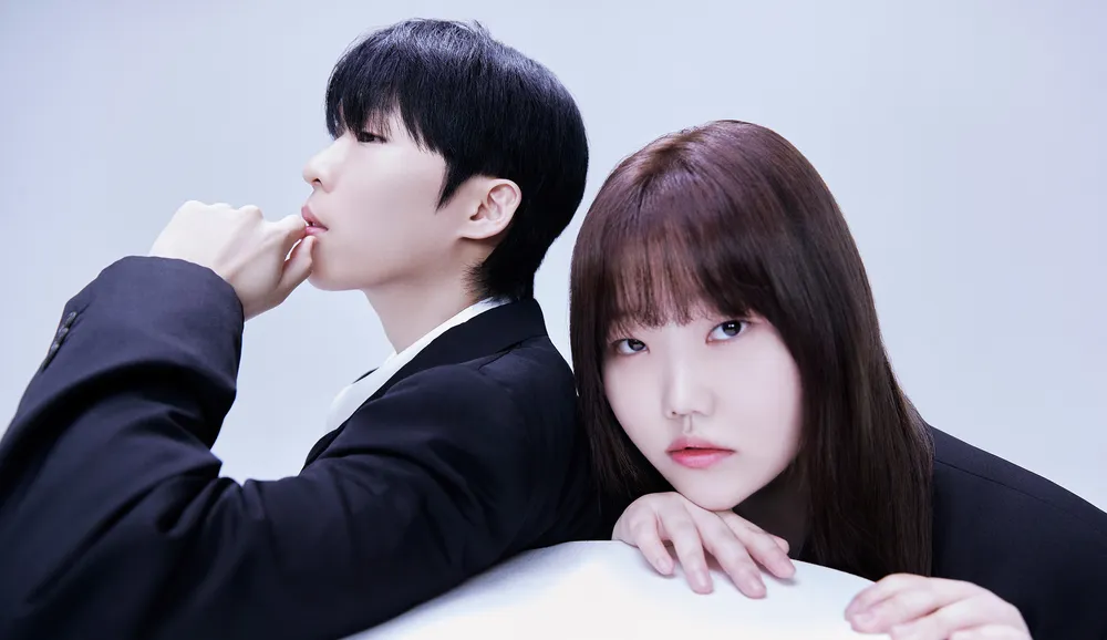 Professional portrait of AKMU, the Korean sibling duo, featuring the two members against a light background with contrasting poses and dark outfits, highlighting their artistic image and signature minimal aesthetic.
